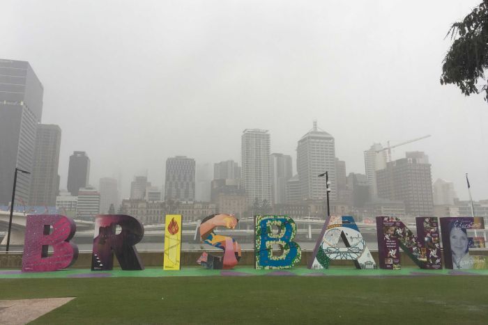 Heavy rain falls, the Brisbane sign in the foreground and the city in the background