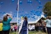 People standing in a circle releasing blue balloons into the sky.