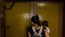 Layla, wearing a pink backpack, holds Tia as she opens the front door to her room.