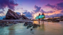 Pink and purple sky over surfers at the beach