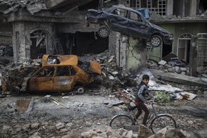 A boy rides his bike past destroyed cars and houses in a neighborhood recently liberated by Iraqi security forces, on the western side of Mosul, Iraq, Sunday, March 19, 2017.