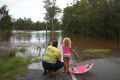 Adam Nelson and daughter Chloe, 5, look out at floodwater near their home outside Jimboomba.