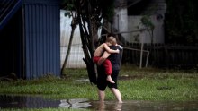 A woman carries a child into her property through ankle-deep water as floodwaters recede in Lismore.