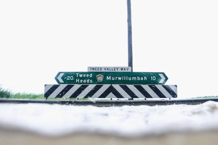 Water level reaches the guard rail at T-intersection road sign for Tweed Heads and Murwillumbah.