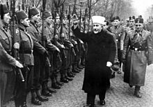 a male dressed in robes reviewing a parade of soldiers