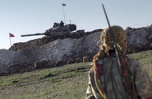 In this February 22, 2015, file photo, a Syrian Kurdish militia member of the YPG patrols near a Turkish army tank as Turks work to build a new Ottoman tomb in the background in Esme village in Aleppo province, Syria.