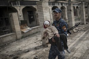 In this Sunday, March 19, 2017 file photo, a federal police officer carries an injured boy through a destroyed train station during fighting between Iraqi security forces and Islamic State militants, on the western side of Mosul, Iraq.