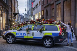 A woman drops flowers onto a police car near the department store Ahlens following a suspected terror attack in central Stockholm, Sweden, Saturday, April 8, 2017.