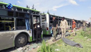 This frame grab from video provided by the Thiqa News Agency, shows rebel gunmen stand at the site of a blast that damaged several buses carrying evacuees, at the Rashideen area, a rebel-controlled district outside Aleppo city, Syria