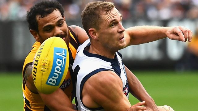 Joel Selwood of the Cats handballs while being tackled by Cyril Rioli of the Hawks.