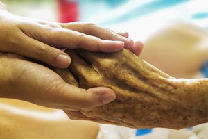 Elderly man hand hugged (helping hand) in a hospice