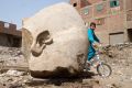 A boy rides his bicycle past the recently discovered statue in a Cairo slum.