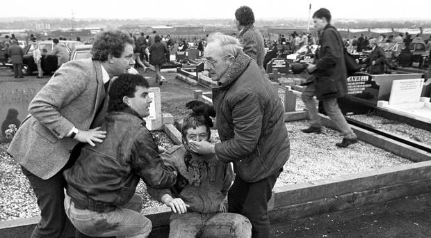 File photo dated 16/03/88 of an injured man being aided by mourners, including Sinn Fein vice president Martin McGuinness (left), at Milltown Cemetery, Belfast, after a gun and bomb attack killed three and left four seriously injured, at the funerals of three IRA members killed in Gibraltar. David Jones/PA Wire