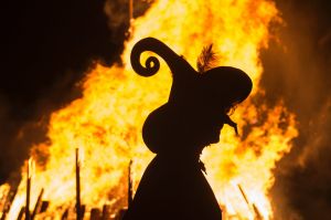 A woman dressed as a witch walks in front of a giant fire during the Walpurgis night in Erfurt, central Germany, Sunday, ...