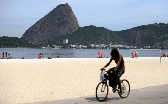 A man rides his bike in the beach in front of the Sugar Loaf Hill in Rio de Janeiro.