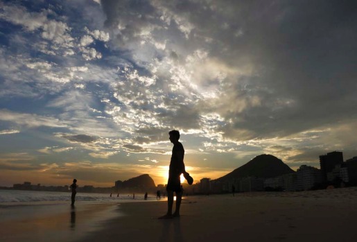 A man stands in the sand during sunset at Copacabana Beach in Rio de Janeiro.