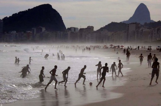 A group of boys play soccer at the edge of the surf at Copacabana Beach.