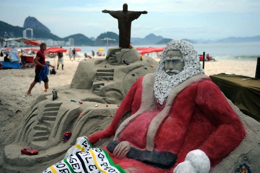 Tourists at Copacabana beach near a sand sculpture depicting Santa Claus in Rio de Janeirro.