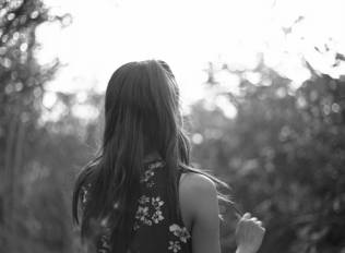 black and white image of back of woman with long hair, facing trees.