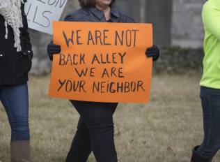 A woman holds a sign protesting bad treatment of addicts.