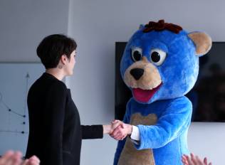 A woman shakes hands with someone in a blue bear character costume.