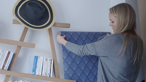 A woman pins up wallpaper on a wall.