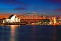 Two of Sydney's famous icons, the Sydney Opera House and Sydney Harbour Bridge lit up at dusk after a vivid sunset.