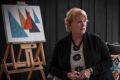 Kerin Kenny sits at home in front of one of her paintings. 