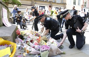 Police and members of the public move floral tributes from St Annes Church to beside a statue in St Annes Square, Manchester, after the terror attack at Manchester Arena, 23rd May 2017.