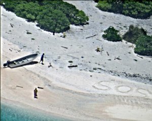 A pair of stranded mariners signal for help by writing "SOS" in the sand as a U.S. Navy P-8A Poseidon aircraft crew from Patrol Squadron (VP) 8 flies over in support of a Coast Guard search and rescue mission, East Fayu Island, Micronesia, 25 August, 2016.