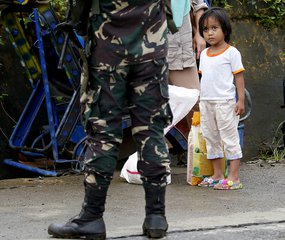 A girl looks at a soldier as people are stopped at a checkpoint while Government forces continue to battle against Muslim militants who lay siege in Marawi city, Saturday, May 27, 2017 in southern Philippines.