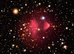 File - This image shows the galaxy cluster 1E 0657-56, also known as the bullet cluster. The optical image from Magellan and HST shows galaxies in orange and white.