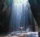 Happy woman traveler with raised arms enjoying life at a beautiful rainforest waterfall in Bali