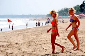 Tourists wearing bikinis walk along Kuta beach in Bali.
