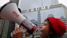 A woman yells on a megaphone and wears a red beanie, a trump property is visible in the background