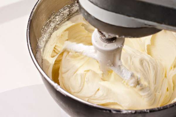 Electric mixer mixing yellow lemon cream cheese cake frosting.  Shot during actual action and features some blur around beater.