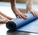 Close-up of attractive young woman folding blue yoga or fitness mat after working out at home in living room. Healthy ...