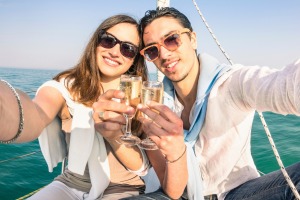 Young couple in love taking selfie on sailing boat cheering with champagne wine - Happy jubilee party cruise travel on ...