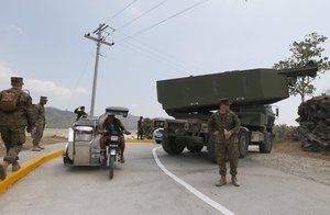 A Filipino worker drives his tricycle past a US-made HIMARS (High Mobility Advanced Rocket System) on a static display after taking part in the 11-day joint US-Philippines military exercise dubbed "Balikatan 2016"