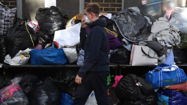 A boy wears a face mask as he walks past clothing, water and food that has been provided at Latymer Church near to the ...