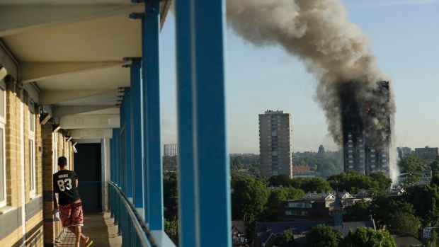 A resident in a nearby building watches smoke rise from the tower on fire in London.