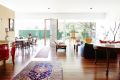 A plywood partition wall separates the kitchen from the open-plan living and dining space, and large glass windows ...