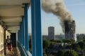 A resident in a nearby building watches smoke rise from the tower on fire in London.