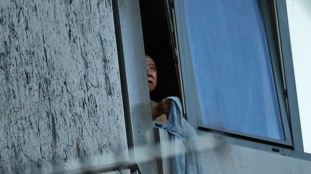 A resident peers out of a window from a small section of the building that was not on fire on Wednesday morning.