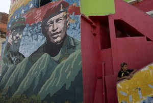 A youth rests on the stairs of his home covered by a mural of Cuba's former President Fidel Castro, left, and Venezuela's late President Hugo Chavez in the 23 de Enero neighborhood of Caracas, Venezuela