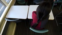 An unidentified child sits alone at a desk in a primary school classroom