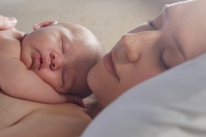 Mother sleeping with newborn baby on bed