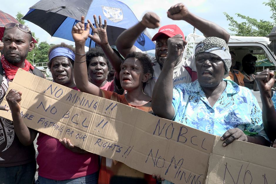 Panguna mine protesters wave their hands and fists in the air and hold a sign that says "No Mining! No BCL!" at a roadblock.