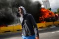 A demonstrator walks near a burning truck during a protest at Francisco Fajardo highway outside La Carlota Air Baise in ...