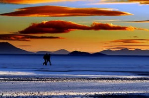 Two people walking across the Salar de Uyuni in Bolivia with fiery sunset  South America.